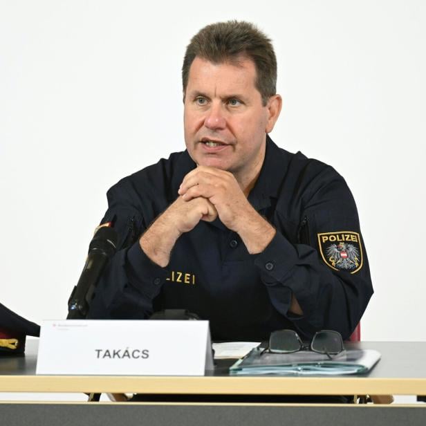 Takács sitzt an einem Tisch mit Mikrofon und Mütze.