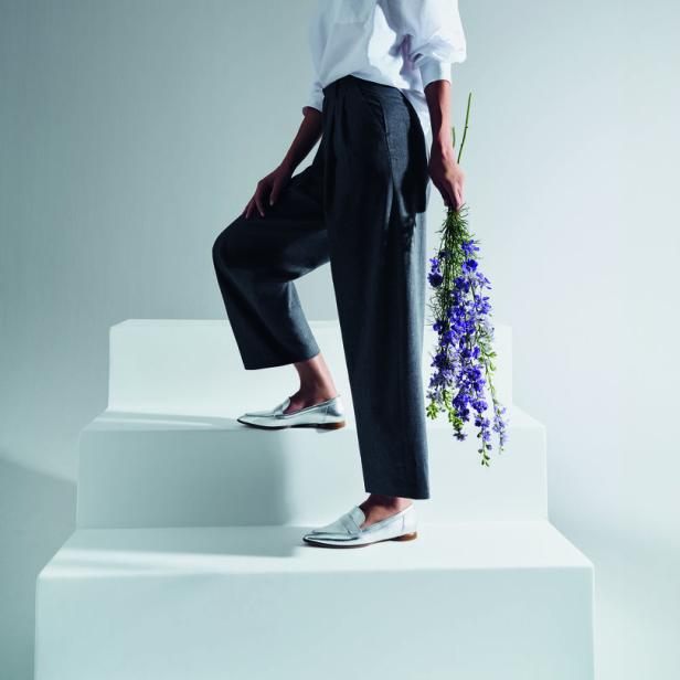 Eine Frau in weißem Hemd und grauer Hose steigt mit einem Blumenstrauß eine weiße Treppe hinauf.