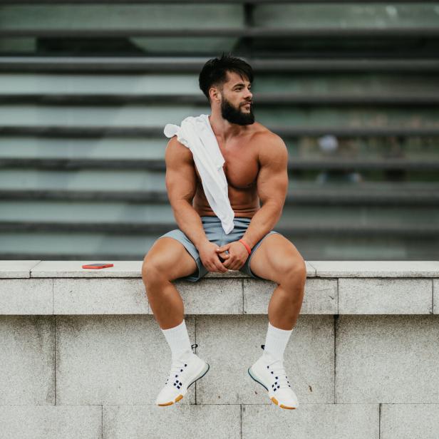 Ein muskulöser Mann entspannt sich nach dem Training im Stadtpark.