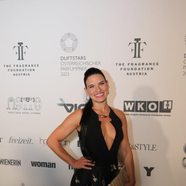 Eine Frau in Abendgarderobe posiert vor einer Wand mit Sponsorenlogos.