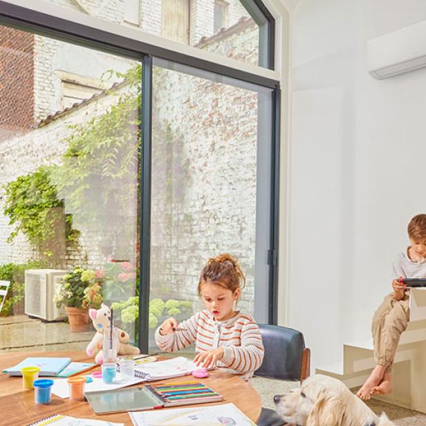 Zwei Kinder spielen in einem Wohnzimmer. Dahinter ist eine Klimaanlage zu sehen.