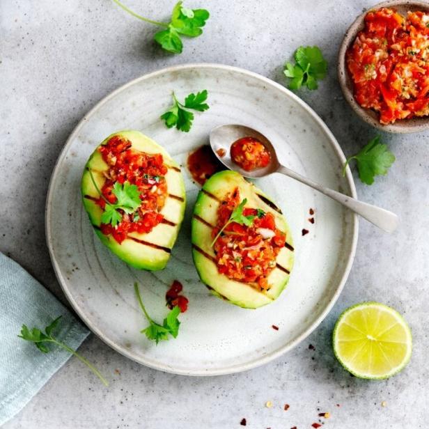Zwei gegrillte Avocadohälften gefüllt mit Tomatensalsa auf einem Teller.