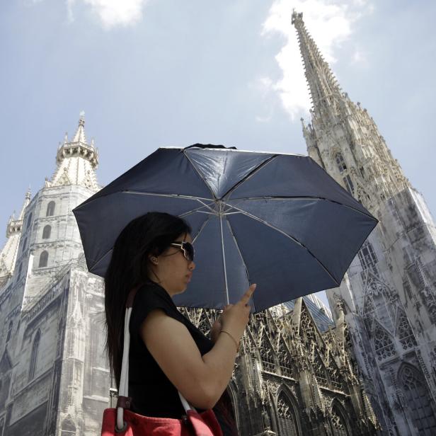 A tourist holds an umbrella in front of St. Stephens cathedral on a sunny day in Vienna