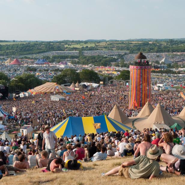 Blick über das Glastonbury Festival mit Menschenmassen, Bühnen und Zelten.