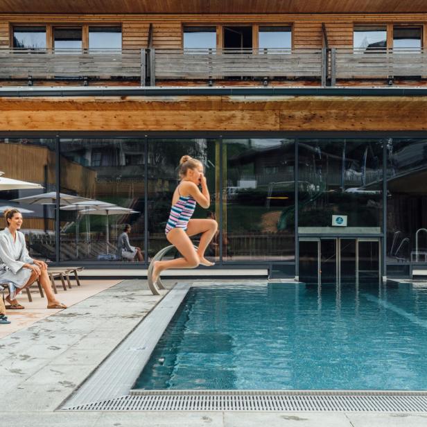 Ein Kind springt in einen Pool vor einem Hotel.