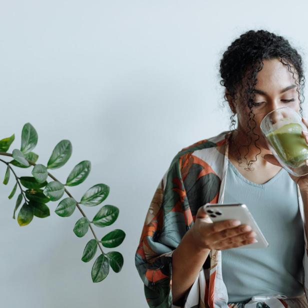 Person trinkt, während sie auf ihr Smartphone blickt, das sie in der Hand hält.