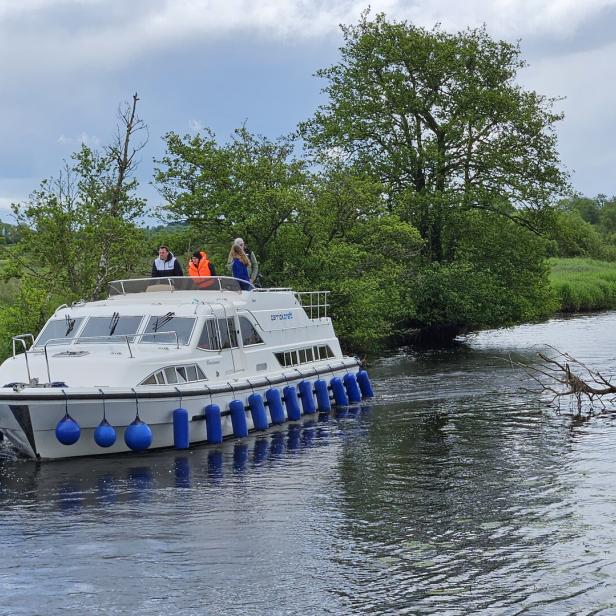 Ein Ausflugsboot fährt auf einem Fluss entlang grüner Ufer.