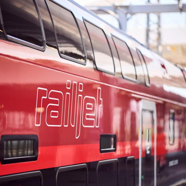 Ein roter Railjet-Zug steht an einem Bahnhof.