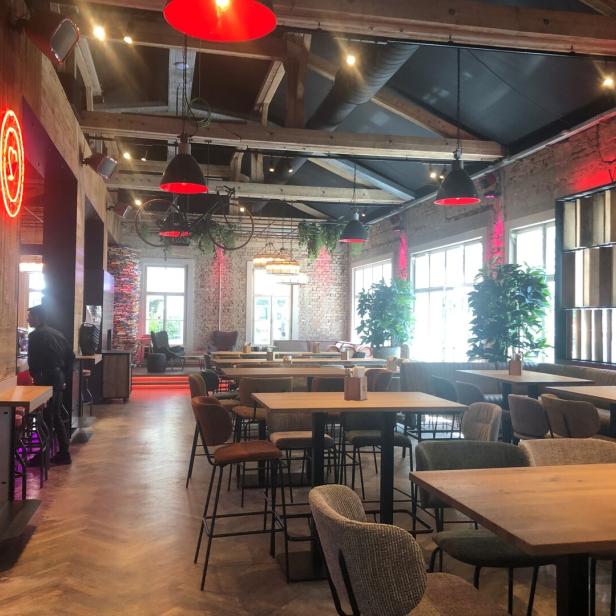 Innenansicht eines Restaurants mit Tischen, Stühlen und dekorativen Elementen wie einem Fahrrad an der Decke.