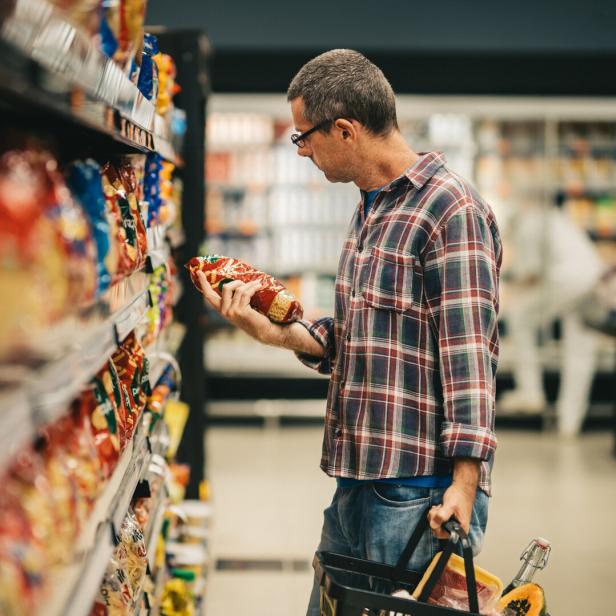 Ein Mann mit Brille und kariertem Hemd betrachtet in einem Supermarkt ein Produkt aus einem Regal.
