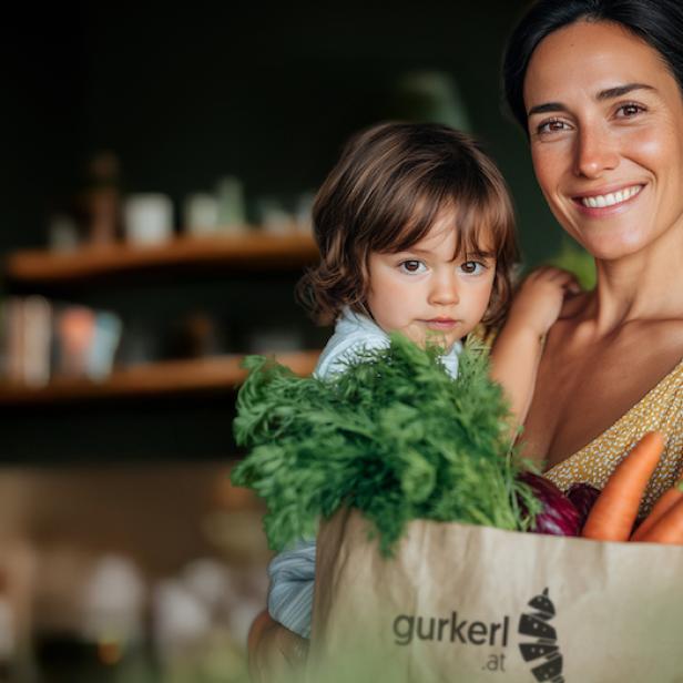 Eine Frau hat ihr Kind auf ihrem Arm und freut sich über ihre Einkaufstüte von gurkerl. 