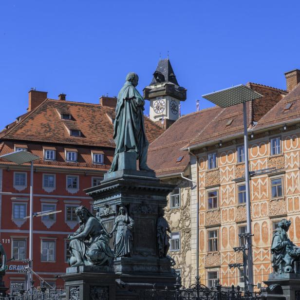 Eine Statue steht vor historischen Gebäuden in Graz, darunter der Grazer Uhrturm.