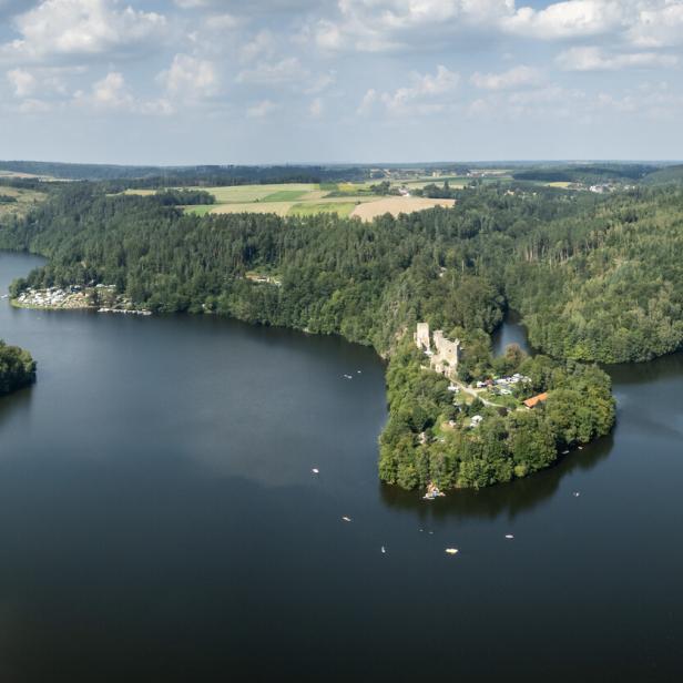 Luftaufnahme einer bewaldeten Landschaft mit einem See und einer Burgruine.