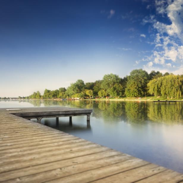 Ein Holzsteg ragt in einen ruhigen See unter blauem Himmel.