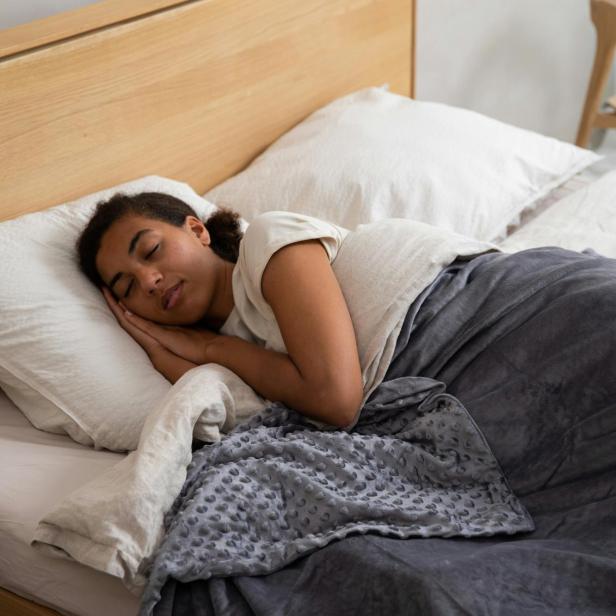 Eine schlafende Frau liegt im Bett, umgeben von weichen Kissen und warmen Decken.