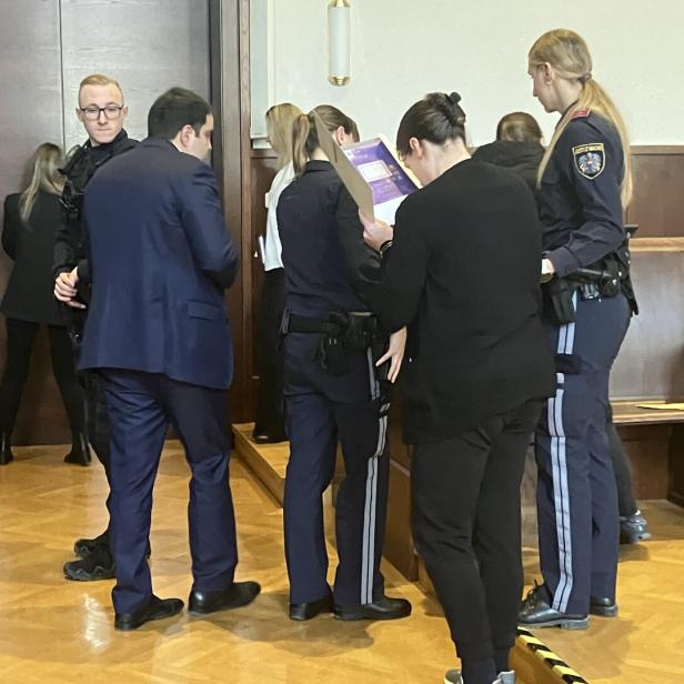 Polizisten stehen in einem Gerichtssaal beisammen und besprechen Dokumente.