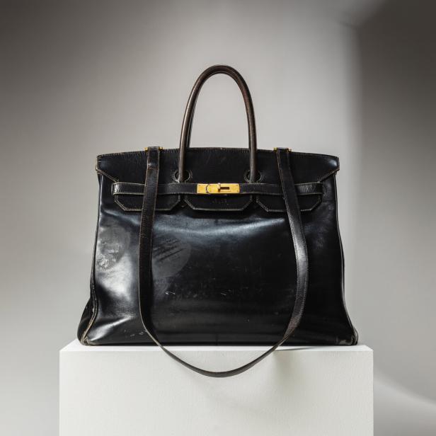 Eine schwarze Birkin Bag von Hermès steht auf einem weißen Sockel.