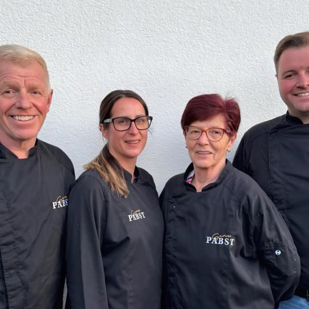 Vier Personen in Kochkleidung lachen in die Kamera.
