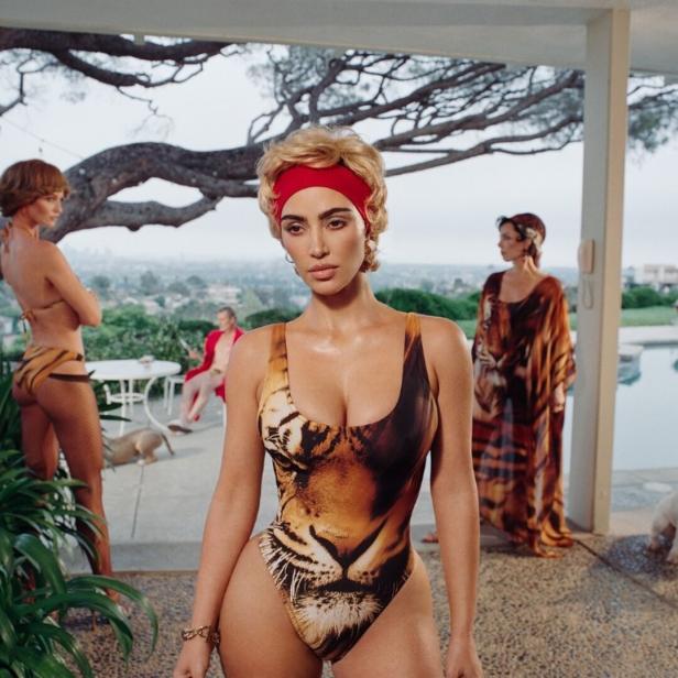 Eine Frau in einem Tiger-Badeanzug posiert mit anderen Models und Hunden an einem Pool.