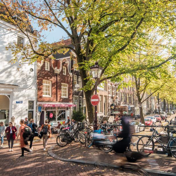 Herbstliche Szene in Amsterdam mit Menschen, Fahrrädern und einem Kanal.