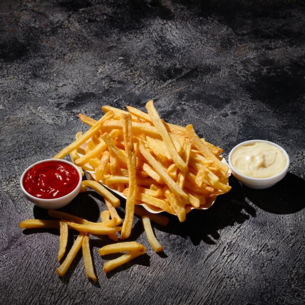 Pommes frites in einem Frittierkorb auf dunklem Hintergrund.
