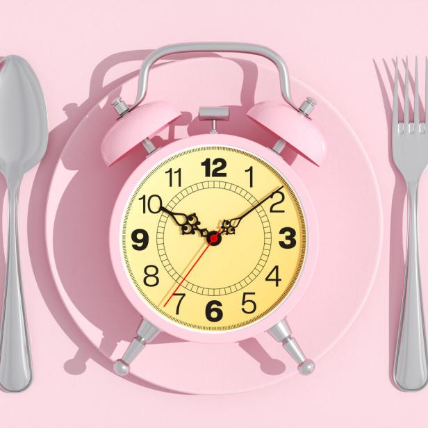 Wecker liegt auf einem Essteller, links und rechts Löffel und Gabel.