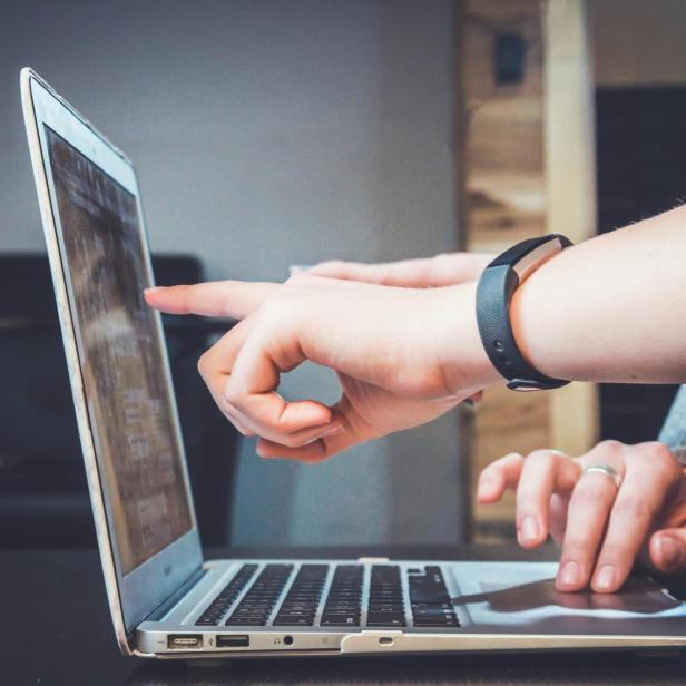 Zwei Personen zeigen mit dem Finger auf einen Laptop