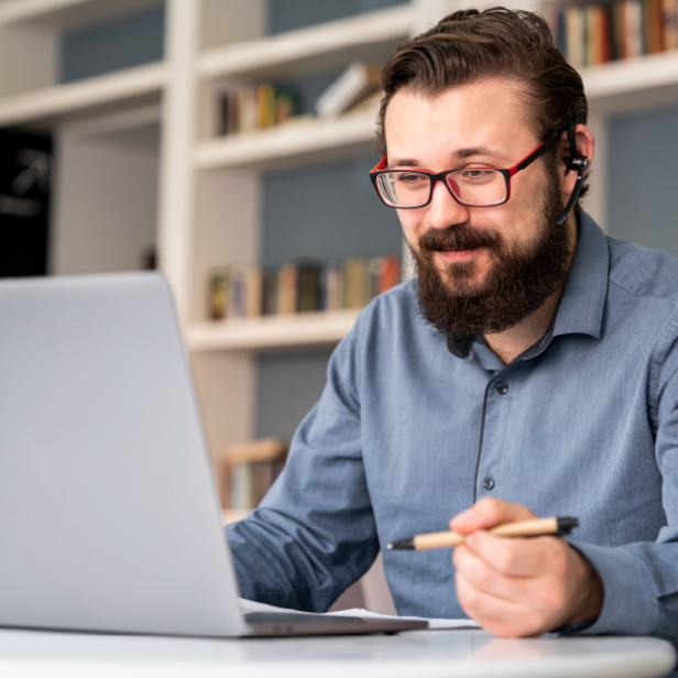 Mann am Laptop mit roter Brille und Stift in der Hand