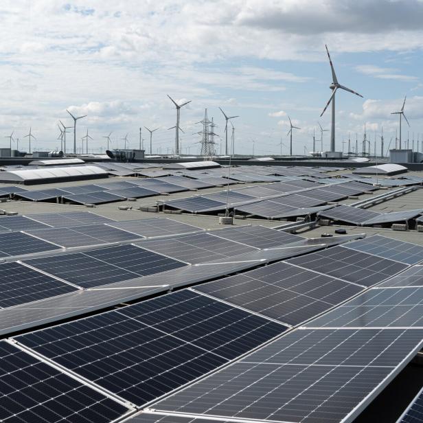 Ein Dach voller Solarzellen mit Windrädern im Hintergrund.