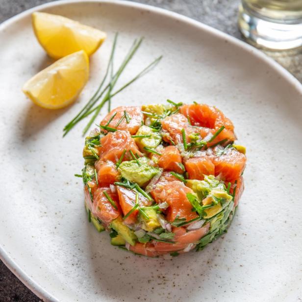 Peruanisches Essen. Lachs-Ceviche mit Avocado, Frühlingszwiebeln und Zitrone auf einem weißen Teller, serviert mit Weißwein.