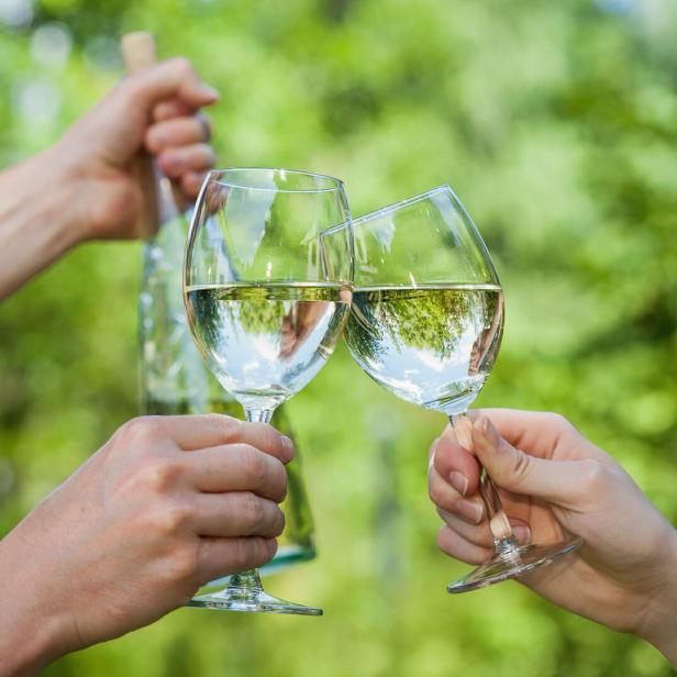 Zwei Personen stoßen mit Weißwein im Freien an.