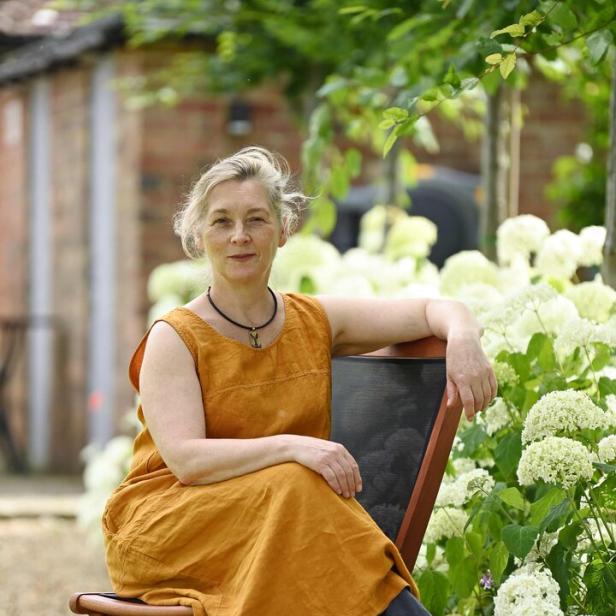 Eine Frau sitzt auf einem Stuhl neben weißen Hortensien in einem Garten.