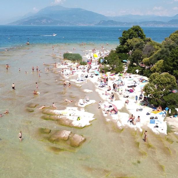 Menschen strömen zu einem der Strände des Gardasees in der südlichen Halbinsel Sirmione.