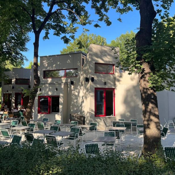 Ein modernes Café mit Außenterrasse und grünen Stühlen unter Bäumen.