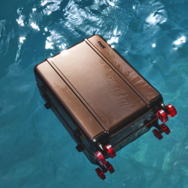 Ein bronzefarbener Rollkoffer treibt auf dem türkisfarbenen Wasser.