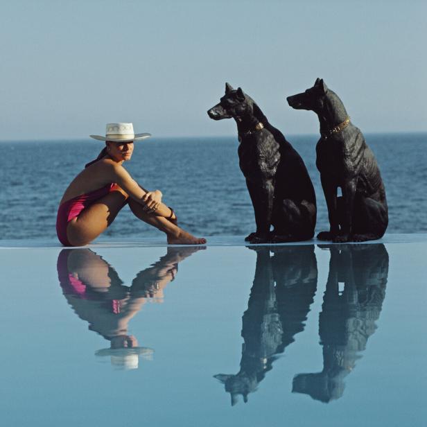Eine Frau sitzt am Pool, hinter ihr liegt das weite Meer.