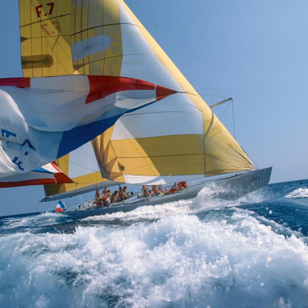 Ein Segelboot mit gelb-weißen Segeln fährt durch aufgewühltes, blaues Wasser.