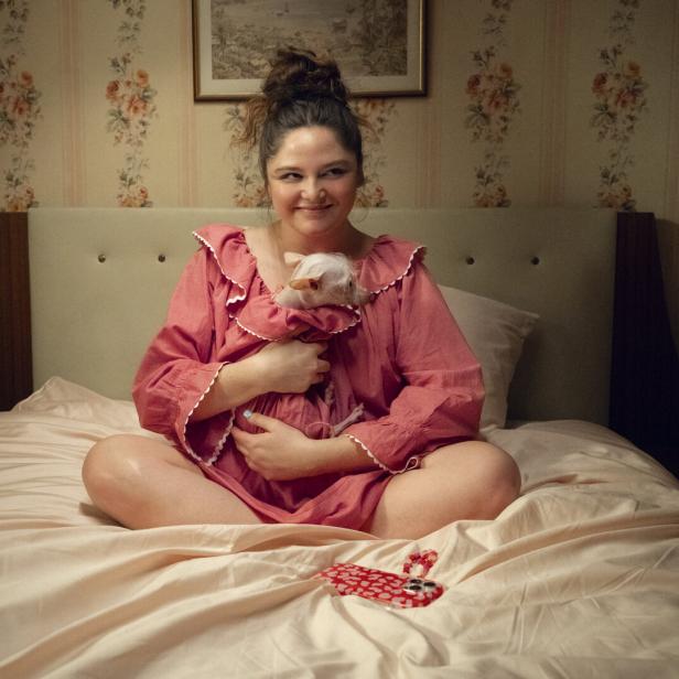 Eine Frau sitzt auf einem Bett und hält ein kleines, weißes Tier im Arm.