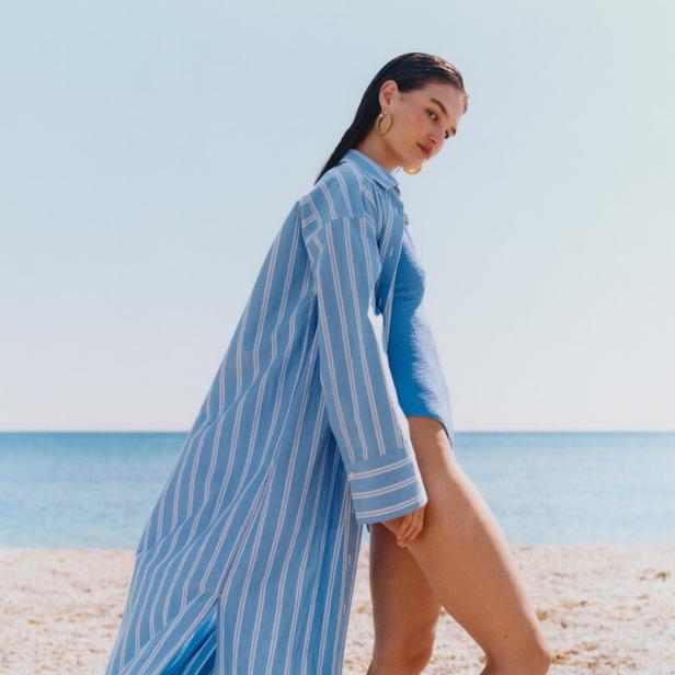 Eine Frau in Badebekleidung und einem blau-weiß gestreiften Hemd am Strand.