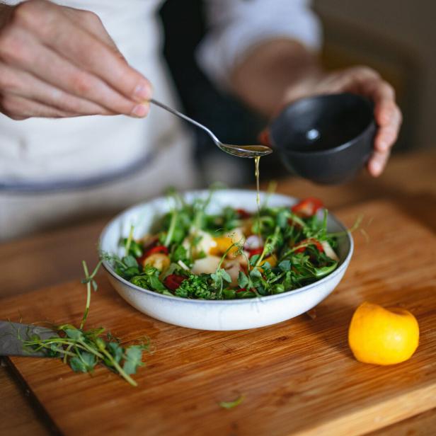 Ein Mann beträufelt einen bunten Salat mit Dressing.