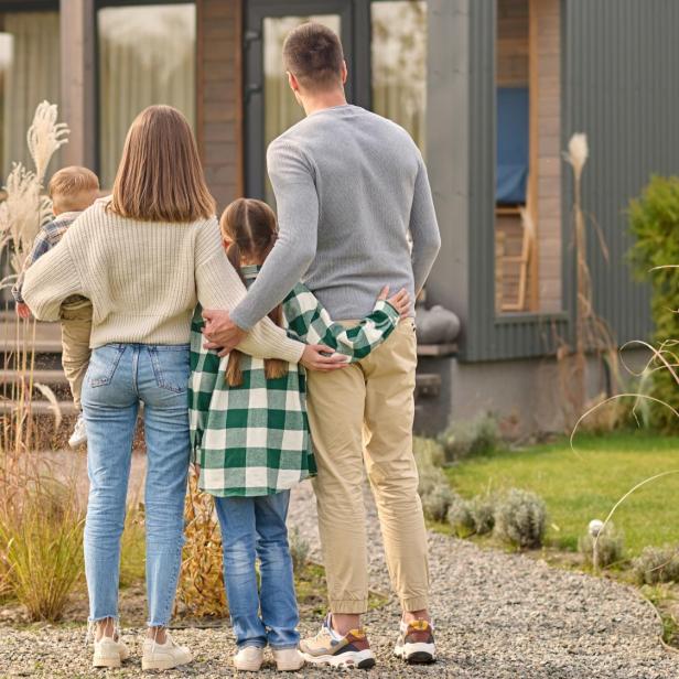 Eine Familie mit zwei Kindern steht vor einem Haus, mit dem Rücken zur Kamera gewandt.