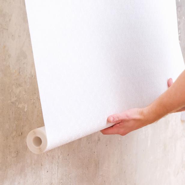 Eine Person klebt eine Tapete an eine Wand.