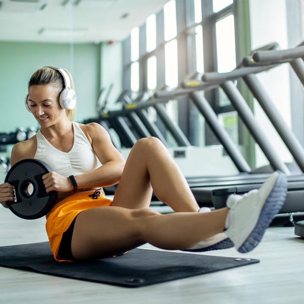 Eine Frau in Sportkleidung trainiert auf einer Matte mit Gewichten und hört mit Kopfhörern Musik.