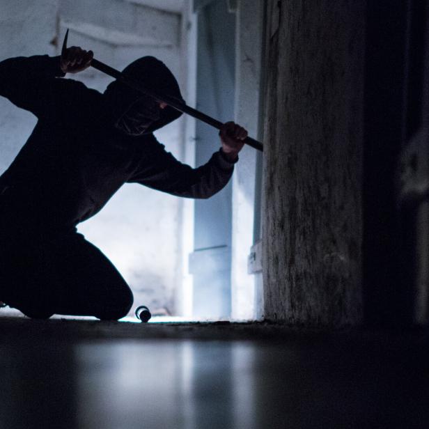 Einbrecher mit Brecheisen in einem dunklen Raum.