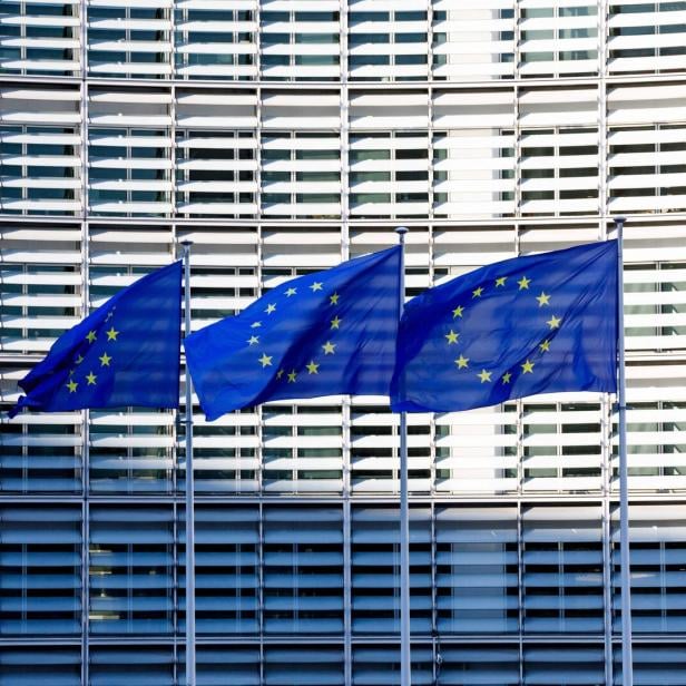 Drei Europaflaggen wehen vor einem modernen Gebäude.