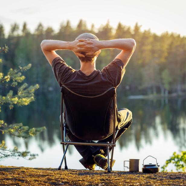 Ein Mann sitzt an einem See in einem Campingstuhl an einem schönen Sommerabend.