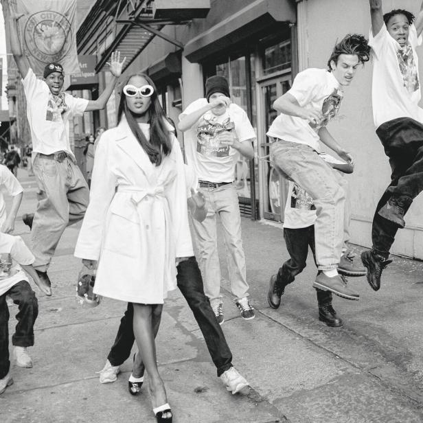 Naomi Campbell auf der Straße, rundherum springen junge Männer und Buben mit Baggy-Pants.