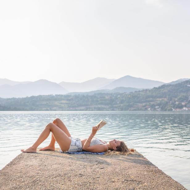 Eine Frau liest ein Buch am See.