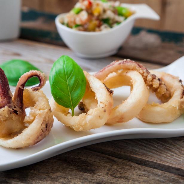 Frittierte Calamari-Ringe mit Basilikum auf einem weißen Teller.