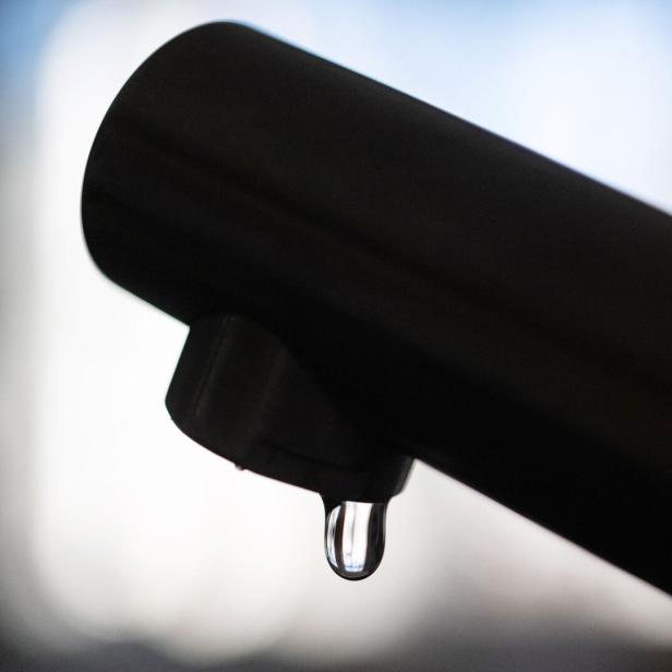 Ein einzelner Wassertropfen hängt an der Spitze eines dunklen Wasserhahns.